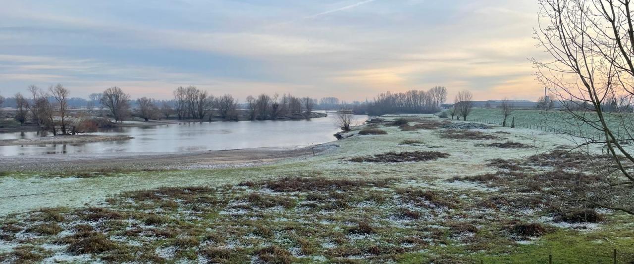 Beautiful winter scene with frost covering fields and river near Tiel, Netherlands at sunset.