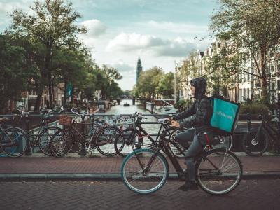 Food delivery cyclist rides through Amsterdam, showcasing urban lifestyle and iconic canals.
