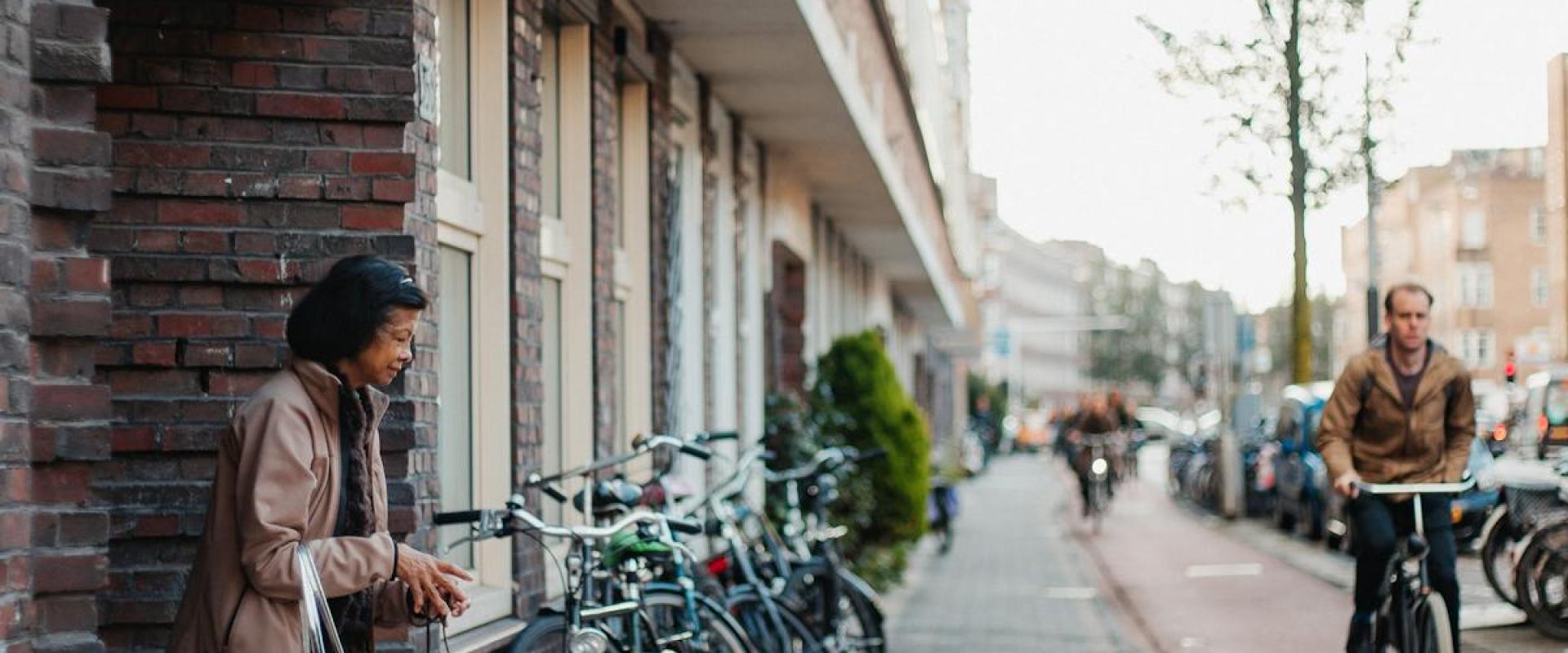 A vibrant street scene in a Dutch neighborhood with people, bicycles, and a small dog.