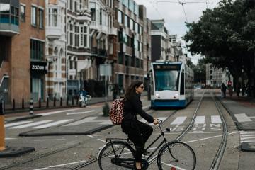 A woman rides a bicycle in Amsterdam with a tram and classic European architecture in view.