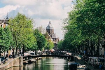 Explore the charming canals and historic architecture of Amsterdam, featuring boats and lush greenery.