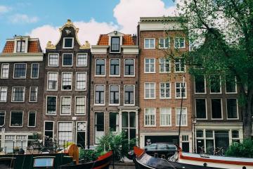 Discover the serene beauty of Amsterdam's iconic canal lined with historic Dutch architecture boats under a clear blue sky.