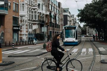 A woman rides a bicycle in Amsterdam with a tram and classic European architecture in view.