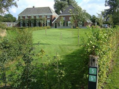 A view of a traditional Dutch brick farmhouse with a thatched roof, set behind a green lawn, with a green trail marker sign (labeled '5' and '5A') in the foreground.