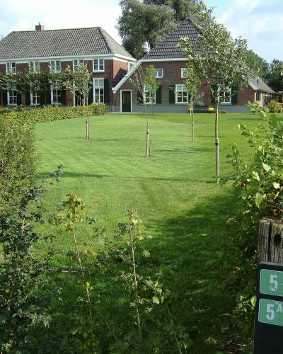 A view of a traditional Dutch brick farmhouse with a thatched roof, set behind a green lawn, with a green trail marker sign (labeled '5' and '5A') in the foreground.