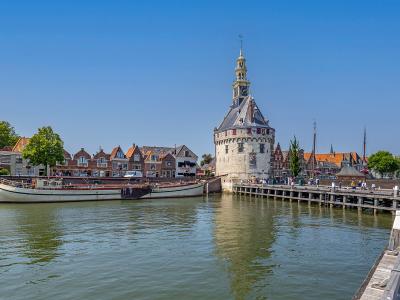 A view of the Hoofdtoren (Main Tower) in Hoorn, Netherlands, standing at the edge of a canal with a traditional boat moored nearby and historic buildings in the background.
