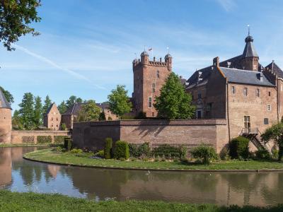 A historic brick castle with a moat, surrounded by greenery, under a clear blue sky.