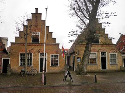 A traditional Dutch brick building with stepped gables, a flagpole, a bicycle, and a sandwich board sign on a cobblestone street.