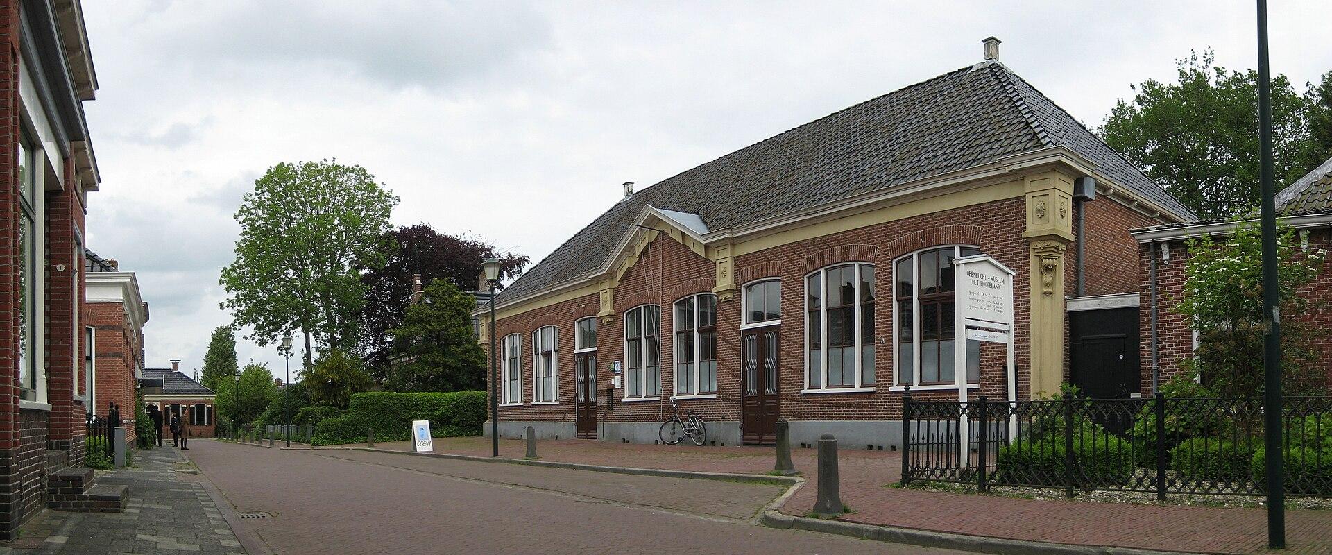 A single-story red brick building with a tiled roof and white-framed windows, featuring a white signboard in front that reads "MUSEUM HET HOOGELAND".