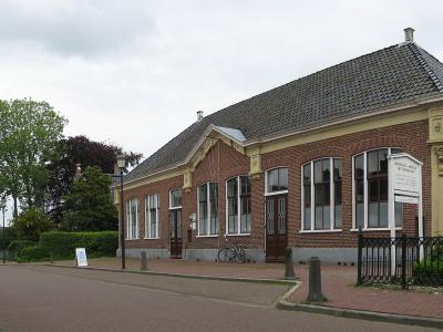 A single-story red brick building with a tiled roof and white-framed windows, featuring a white signboard in front that reads "MUSEUM HET HOOGELAND".