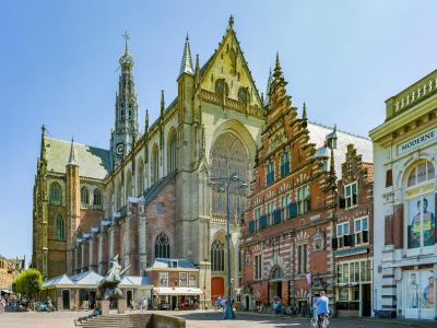The image shows the St. Bavokerk (Grote Kerk) in Haarlem, Netherlands, featuring its distinctive late Gothic architecture, tall spire, and adjacent historic buildings on the Grote Markt square.