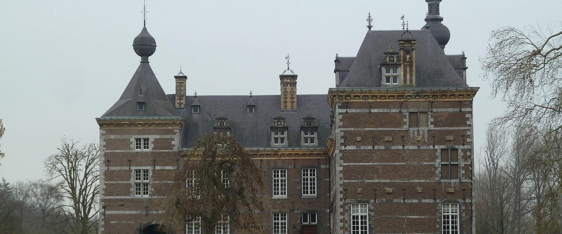 A large brick castle with distinctive onion-domed towers and a central courtyard, set behind a green lawn under an overcast sky.