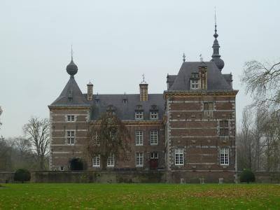 A large brick castle with distinctive onion-domed towers and a central courtyard, set behind a green lawn under an overcast sky.