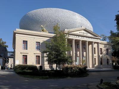 A neoclassical building with a large silver dome and a golden sculpture on the roof, with "MUSEUM DE FUNDATIE" inscribed on the pediment.