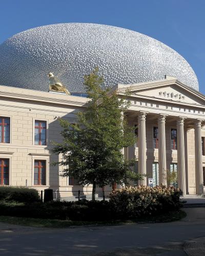 A neoclassical building with a large silver dome and a golden sculpture on the roof, with "MUSEUM DE FUNDATIE" inscribed on the pediment.