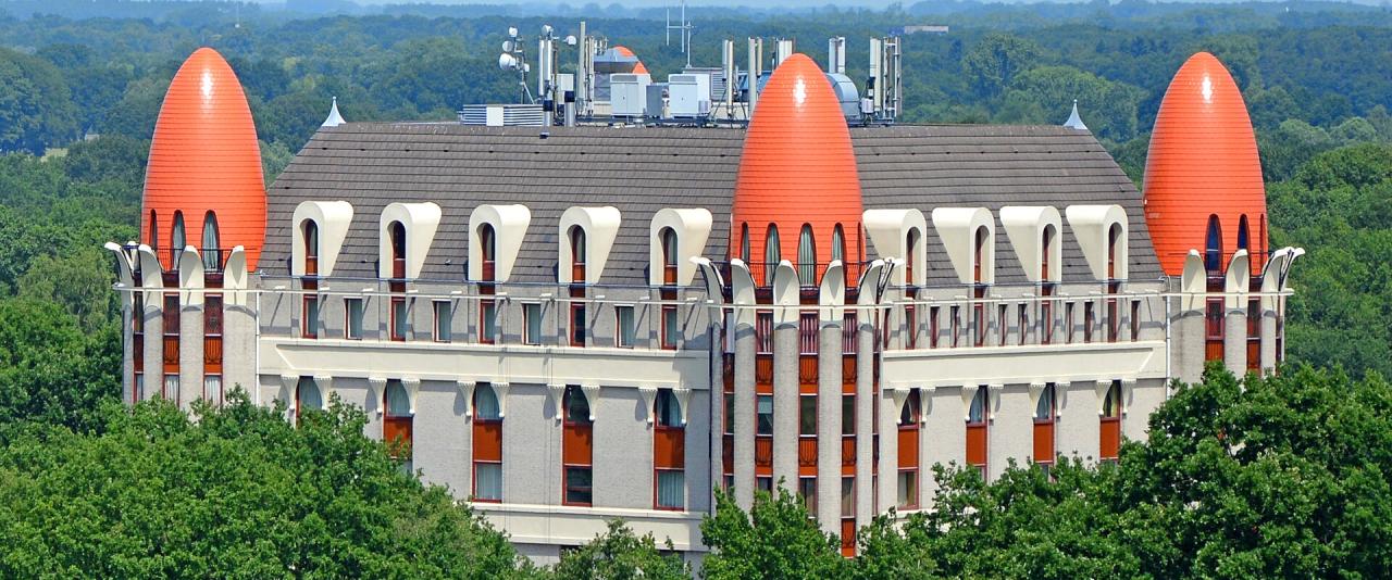 1. A large hotel building with distinctive orange, egg-shaped towers and a grey roof, surrounded by dense green trees under a clear blue sky.