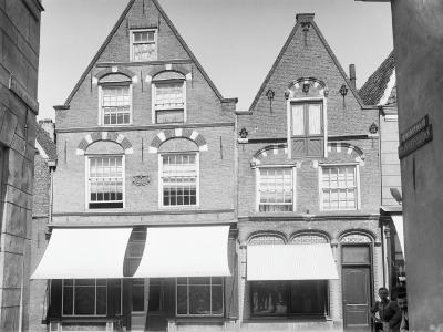 A black and white photograph showing the facades of two adjacent brick buildings with stepped gables and awnings over ground-floor shop windows, with a street sign on the right reading "MUNSTRAAT".