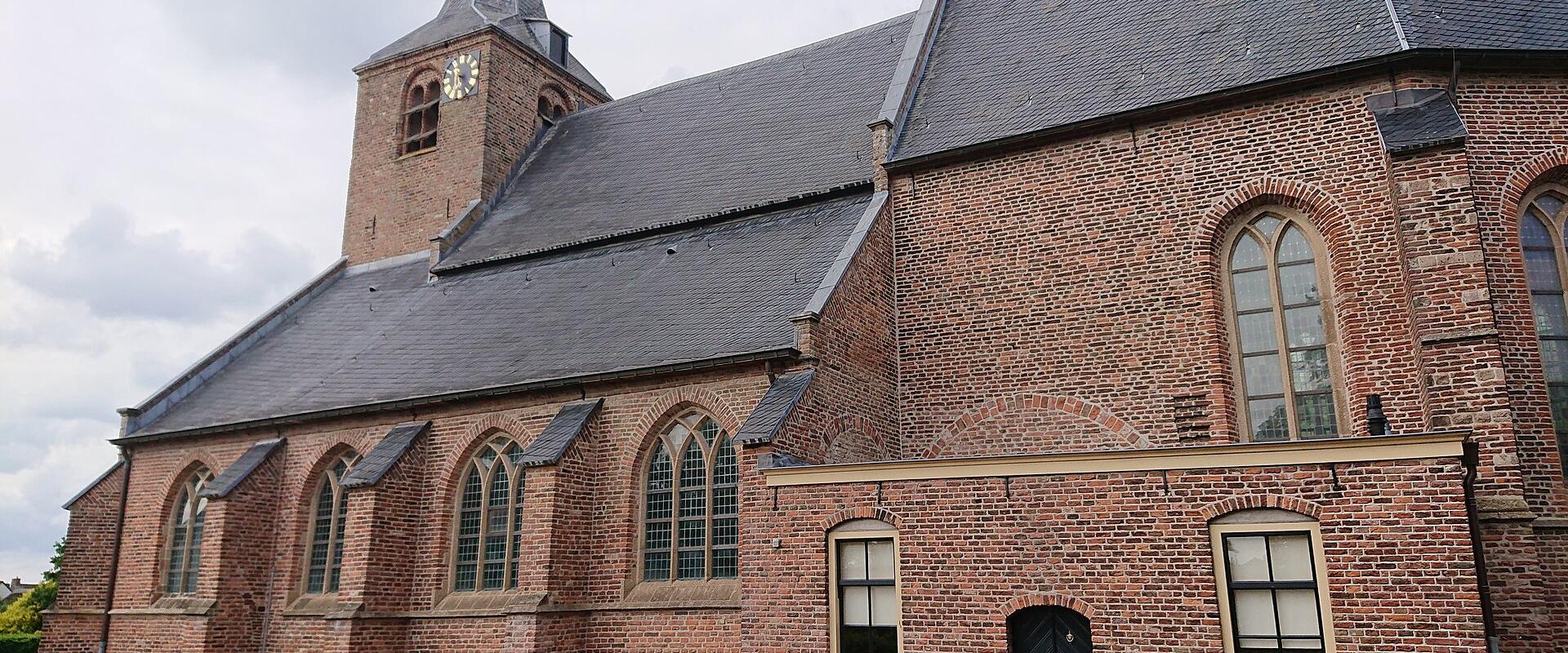 A red brick church with a slate roof and a small spire featuring a clock face, set against a cloudy sky.