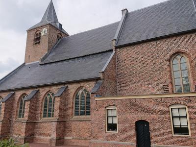 A red brick church with a slate roof and a small spire featuring a clock face, set against a cloudy sky.