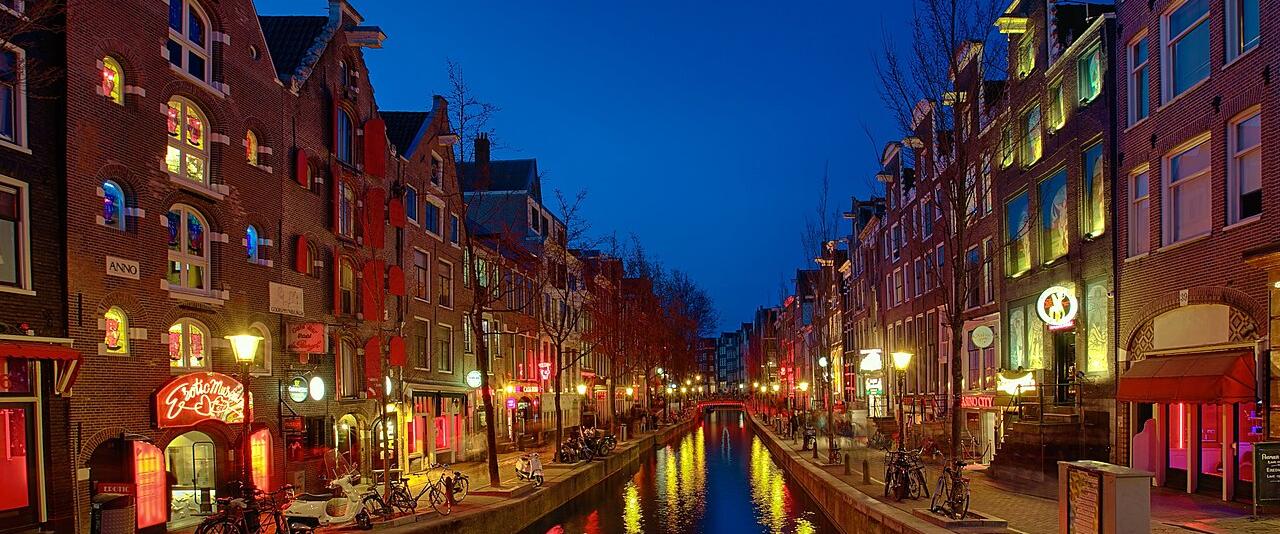 Oudezijds Achterburgwal canal in the Red Light District at dusk, reflecting red and yellow window lights