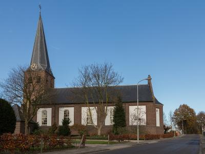 The image shows a brick church with a tall, slender, dark-slated spire, white-painted rectangular panels on the nave, and a street lamp in the foreground.