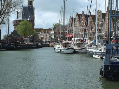 A black-and-white photograph printed in a book showing a historic stone gatehouse tower (the Drommedaris) standing at the edge of a harbor with boats and trees in the background.