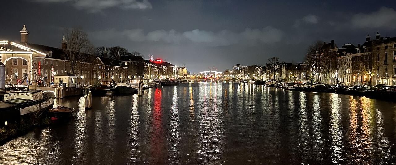The Amstel river in Amsterdam at night with lit bridges and canal houses reflected in the water