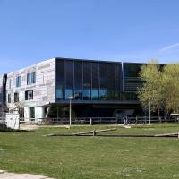 1. A modern, angular building with a grey tiled facade and large glass windows, situated next to a grassy area with wooden logs and a brick chimney in the background.