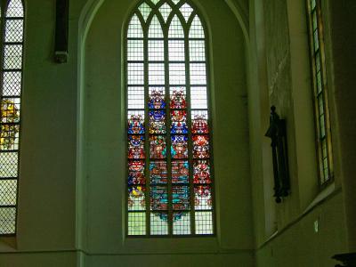 Interior view of a large church hall featuring tall Gothic arched windows with stained glass, a dark wooden ceiling, and a shop area at the bottom with a sign reading "WERELDWINKEL".