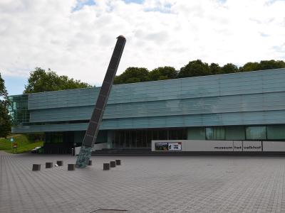 A modern glass-fronted building with a large leaning sculpture in front, featuring signage that reads "museum het valkhof".