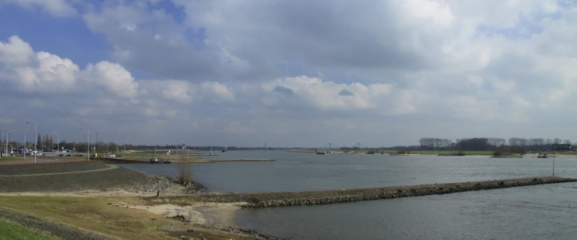 The broad Waal river with its groynes and riverbanks under a cloudy sky
