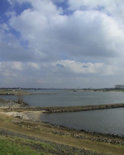 The broad Waal river with its groynes and riverbanks under a cloudy sky