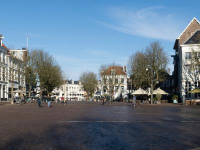 A wide, paved public square (brink) lined with historic Dutch buildings, trees, and outdoor cafe seating under a blue sky.