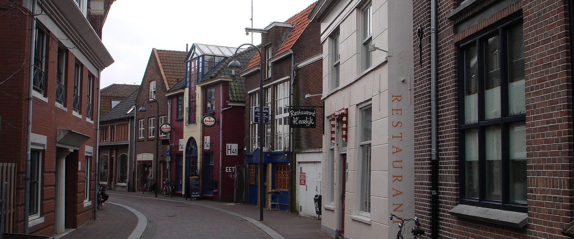 A street-level view of a brick building housing a tobacco shop ("Tabaksspeciaalzaak Joop Heij") with a blue street sign reading "Joop Heijplein".