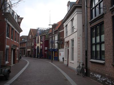 A street-level view of a brick building housing a tobacco shop ("Tabaksspeciaalzaak Joop Heij") with a blue street sign reading "Joop Heijplein".