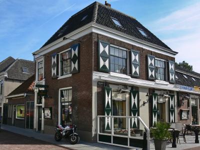 A wide, paved pedestrian square lined with historic Dutch-style buildings, bare trees, and street lamps under a blue sky, with a distinctive building featuring a small tower or cupola visible in the center distance.