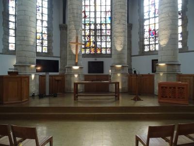 The image shows the interior of a large church featuring massive cylindrical stone pillars, tall stained-glass windows, and a wooden altar area with a cross.