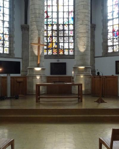 The image shows the interior of a large church featuring massive cylindrical stone pillars, tall stained-glass windows, and a wooden altar area with a cross.